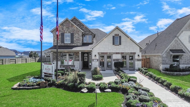 view of front of property featuring a front yard, fence, french doors, and stone siding