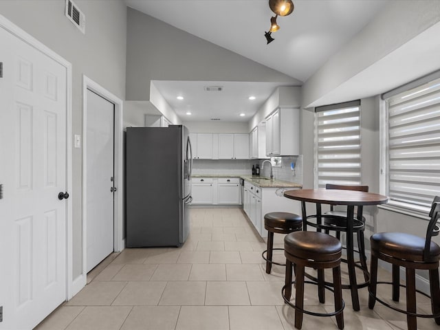 kitchen featuring sink, white cabinetry, vaulted ceiling, stainless steel fridge, and light stone countertops