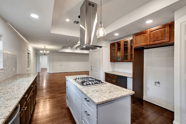 kitchen featuring light stone counters, appliances with stainless steel finishes, a raised ceiling, island exhaust hood, and white cabinets