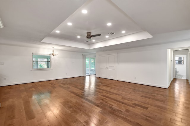 empty room with ceiling fan with notable chandelier, dark wood-type flooring, and a raised ceiling