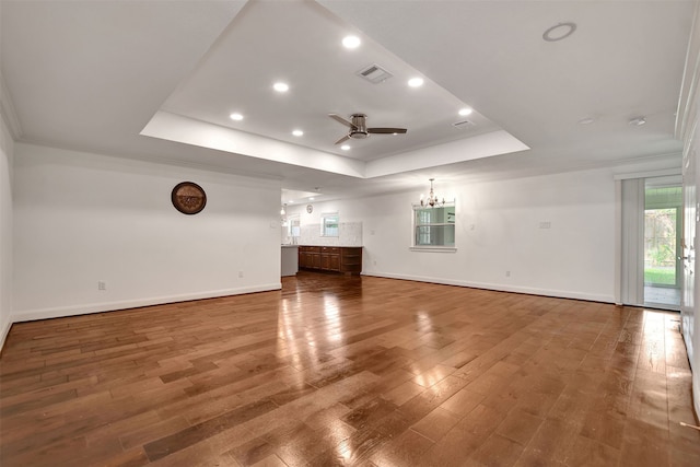 unfurnished living room featuring hardwood / wood-style floors, ceiling fan with notable chandelier, ornamental molding, and a raised ceiling