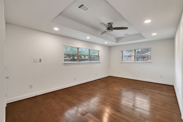 spare room featuring dark wood-type flooring, ceiling fan, and a raised ceiling