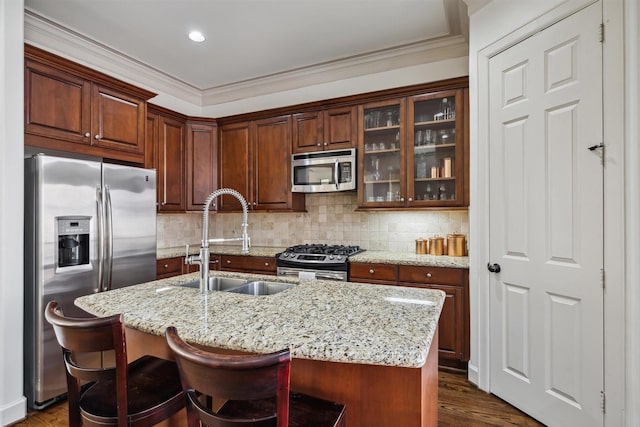 kitchen with sink, appliances with stainless steel finishes, tasteful backsplash, light stone countertops, and a center island with sink