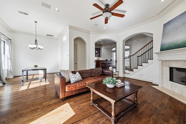 living room featuring dark wood-type flooring, a high end fireplace, crown molding, and ceiling fan with notable chandelier