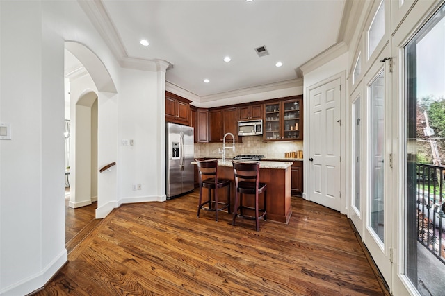 kitchen featuring dark hardwood / wood-style floors, appliances with stainless steel finishes, a kitchen bar, and a kitchen island with sink