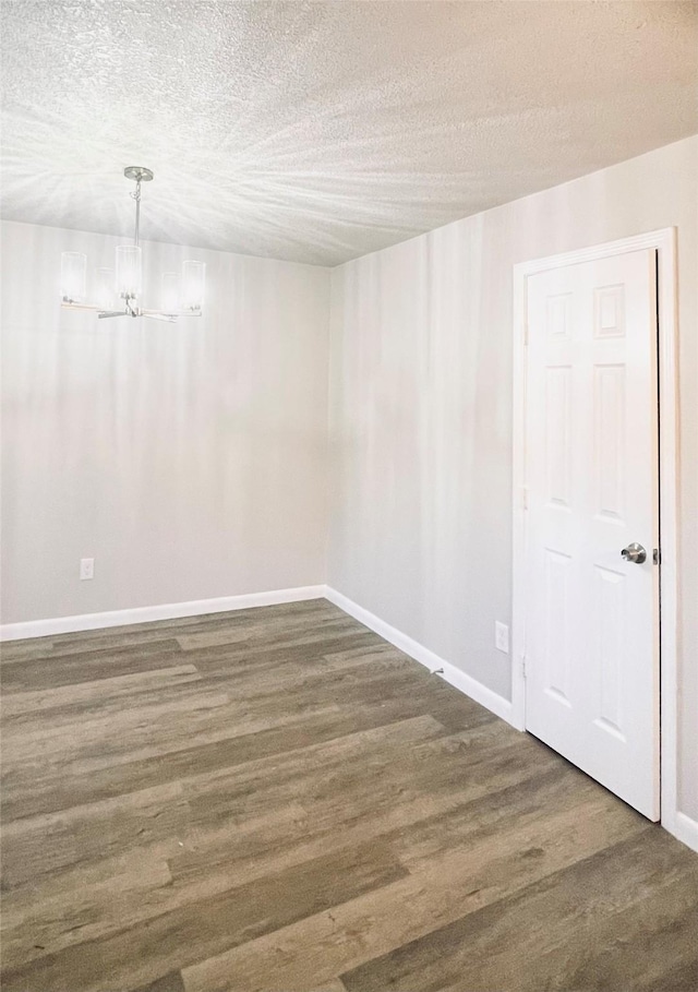 empty room featuring an inviting chandelier, dark hardwood / wood-style flooring, and a textured ceiling