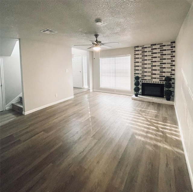 unfurnished living room with dark wood-type flooring, ceiling fan, a brick fireplace, and a textured ceiling