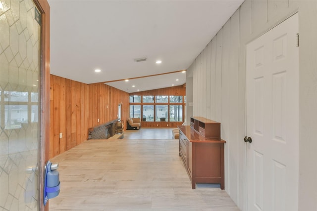 hall featuring vaulted ceiling, wood walls, and light hardwood / wood-style flooring