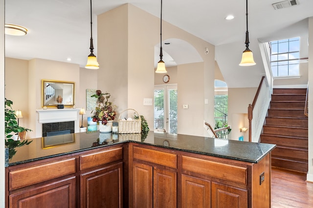 kitchen featuring hanging light fixtures, dark stone countertops, a fireplace, and light wood-type flooring