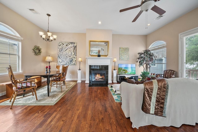 living room featuring dark wood-type flooring, ceiling fan with notable chandelier, and a tile fireplace