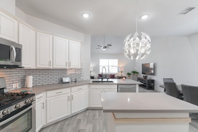 kitchen featuring appliances with stainless steel finishes, decorative light fixtures, white cabinetry, sink, and a center island