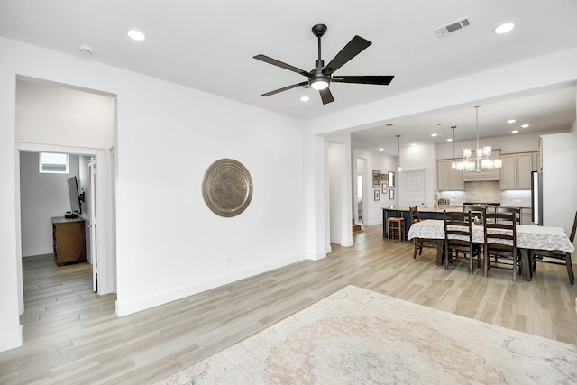 living room with ceiling fan with notable chandelier and light wood-type flooring