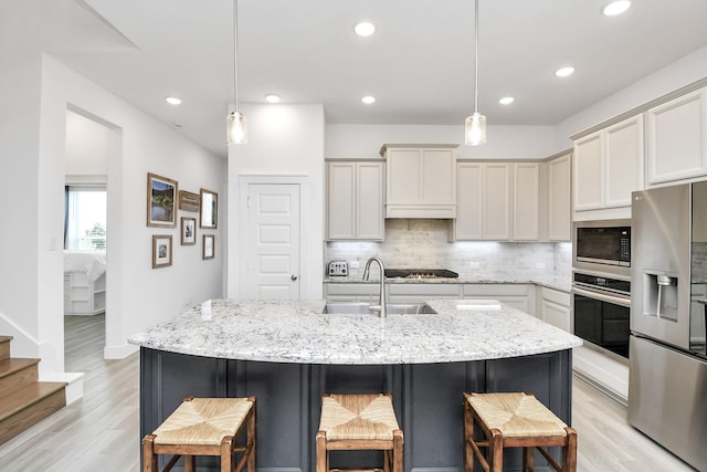 kitchen featuring appliances with stainless steel finishes, sink, hanging light fixtures, a kitchen island with sink, and light stone countertops