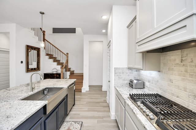 kitchen featuring appliances with stainless steel finishes, sink, decorative backsplash, hanging light fixtures, and light stone countertops