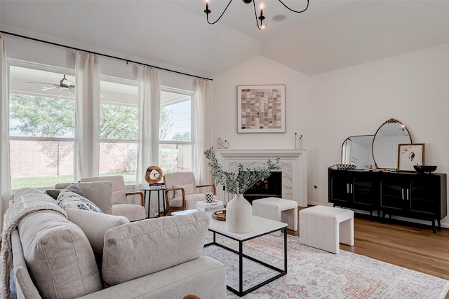 living room with a high end fireplace, vaulted ceiling, light hardwood / wood-style floors, and ceiling fan with notable chandelier