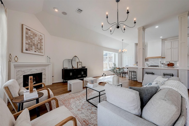 living room featuring lofted ceiling, hardwood / wood-style floors, a notable chandelier, and a fireplace