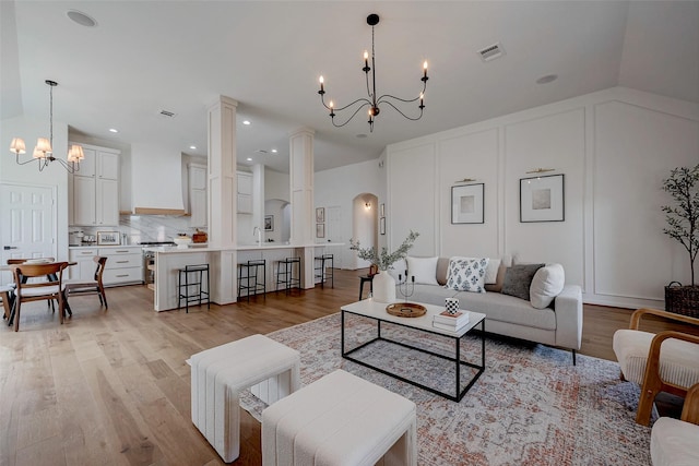 living room with ornate columns, vaulted ceiling, a chandelier, and light hardwood / wood-style flooring