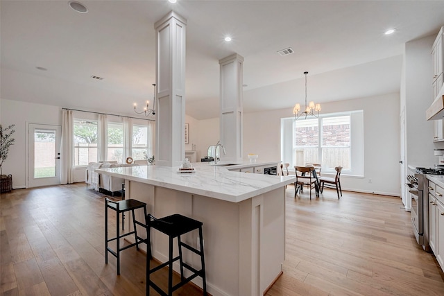 kitchen with white cabinetry, a chandelier, hanging light fixtures, light stone countertops, and high end stove