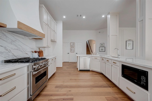 kitchen featuring white cabinets, custom exhaust hood, stainless steel appliances, light stone countertops, and light hardwood / wood-style flooring