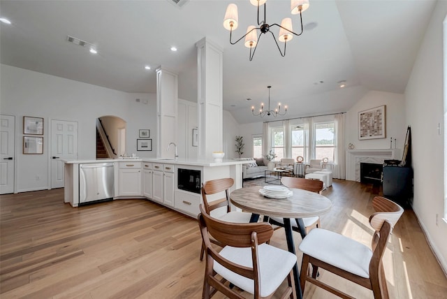 dining space featuring sink, light hardwood / wood-style flooring, a premium fireplace, vaulted ceiling, and a chandelier