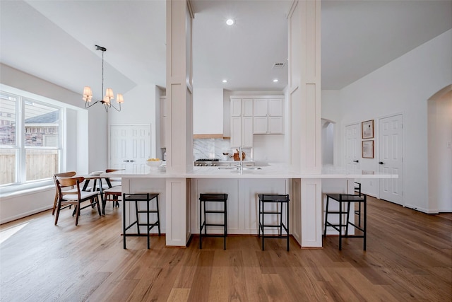 kitchen with hanging light fixtures, white cabinets, a kitchen breakfast bar, and wall chimney exhaust hood