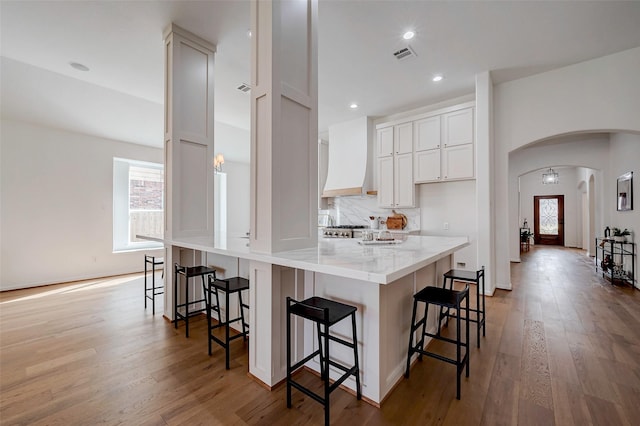 kitchen featuring white cabinetry, light stone countertops, custom range hood, and a breakfast bar area