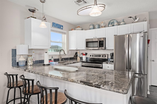 kitchen featuring sink, white cabinetry, hanging light fixtures, stainless steel appliances, and dark stone counters