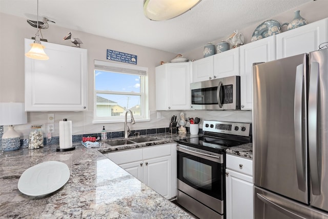 kitchen with pendant lighting, sink, appliances with stainless steel finishes, white cabinetry, and dark stone counters