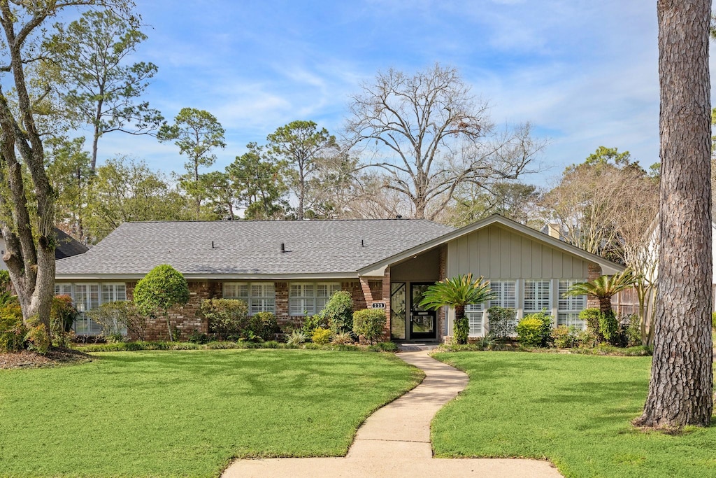view of front facade featuring brick siding, a shingled roof, and a front yard