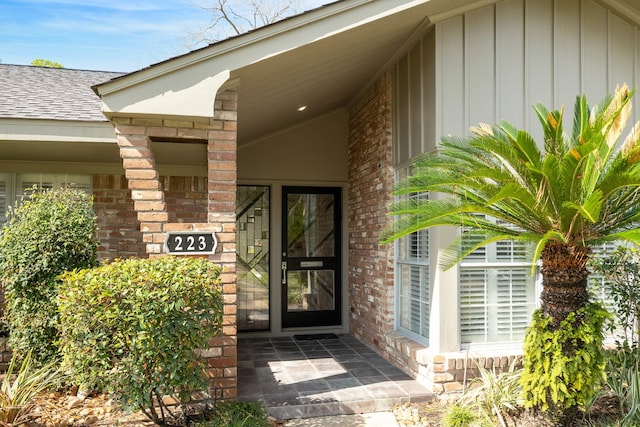 doorway to property with brick siding, board and batten siding, and roof with shingles