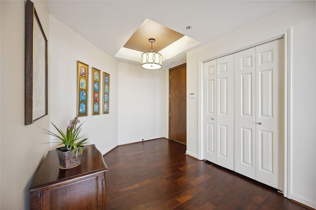 corridor with a tray ceiling and dark wood-type flooring