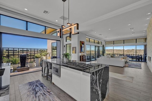 kitchen with pendant lighting, stainless steel gas stovetop, white cabinets, dark stone counters, and a healthy amount of sunlight