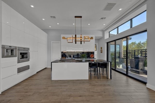 kitchen with pendant lighting, a high ceiling, light hardwood / wood-style floors, white cabinets, and stainless steel oven