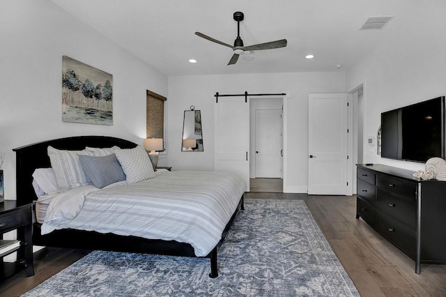 bedroom featuring dark hardwood / wood-style floors, a barn door, and ceiling fan