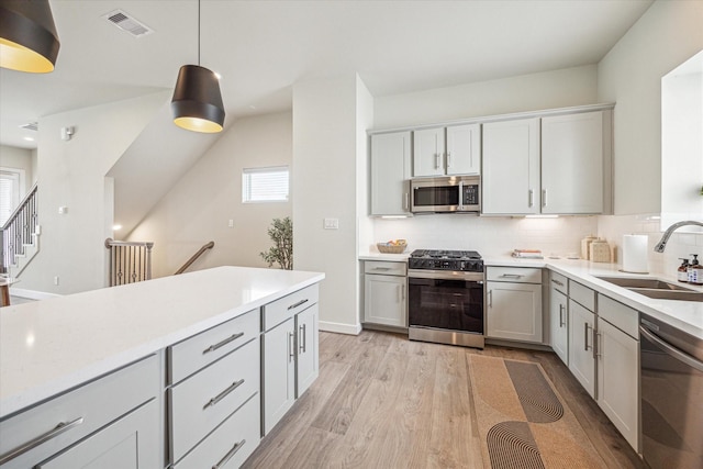 kitchen featuring appliances with stainless steel finishes, decorative light fixtures, sink, gray cabinetry, and light hardwood / wood-style flooring