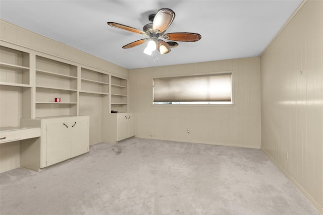 unfurnished bedroom with built in desk, light colored carpet, and ceiling fan