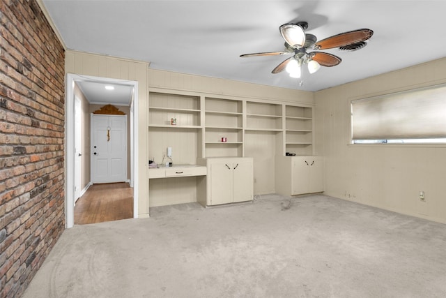 interior space with built in desk, ceiling fan, and brick wall