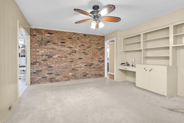 interior space featuring brick wall, built in desk, light colored carpet, and ceiling fan