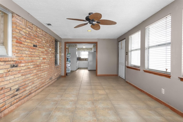 unfurnished room with ceiling fan, a textured ceiling, and brick wall