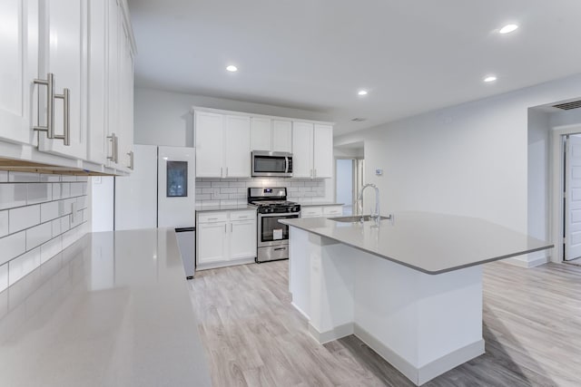 kitchen with sink, light wood-type flooring, appliances with stainless steel finishes, a kitchen island with sink, and white cabinets