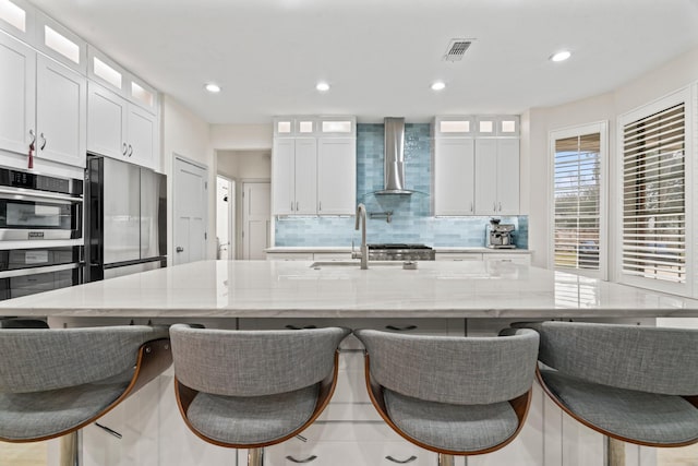 kitchen featuring a large island, wall chimney range hood, light stone counters, and stainless steel refrigerator