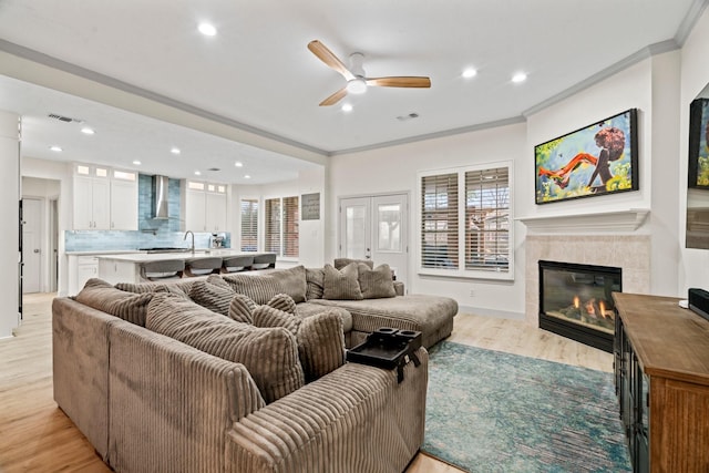 living room featuring a tiled fireplace, crown molding, light hardwood / wood-style flooring, and ceiling fan