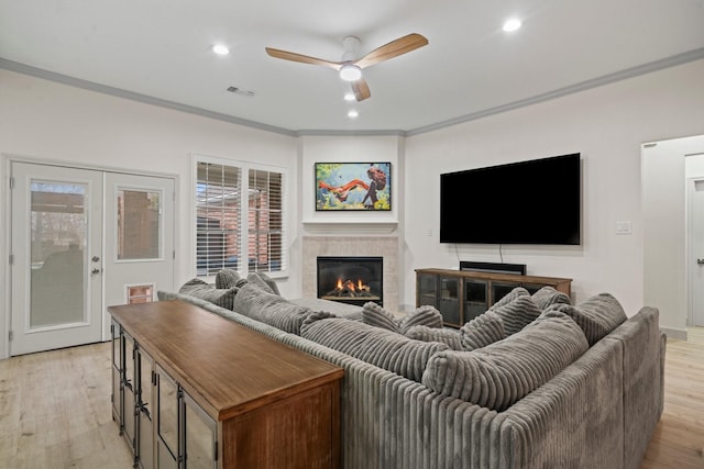 living room with crown molding, ceiling fan, a fireplace, french doors, and light wood-type flooring