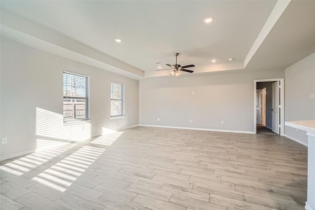 unfurnished room featuring a tray ceiling, light hardwood / wood-style floors, and ceiling fan