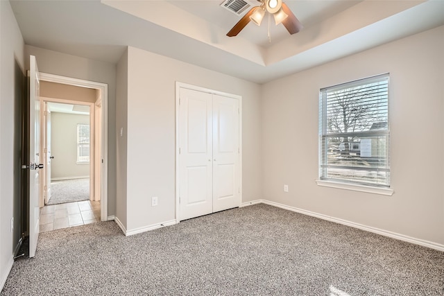 unfurnished bedroom featuring multiple windows, a closet, a raised ceiling, and carpet