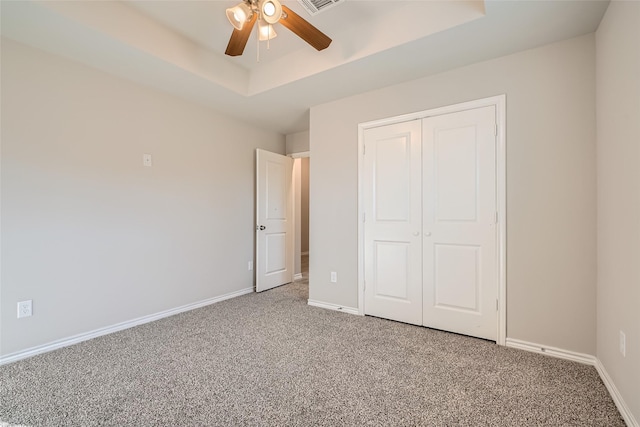 unfurnished bedroom featuring ceiling fan, a tray ceiling, carpet floors, and a closet