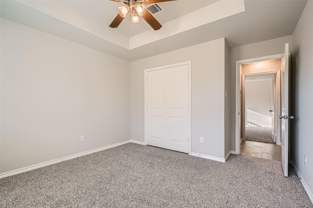 unfurnished bedroom with a closet, light colored carpet, ceiling fan, and a tray ceiling