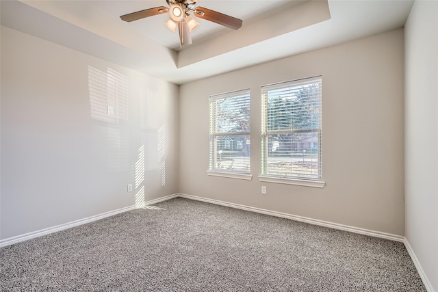 empty room with ceiling fan, a tray ceiling, and carpet floors