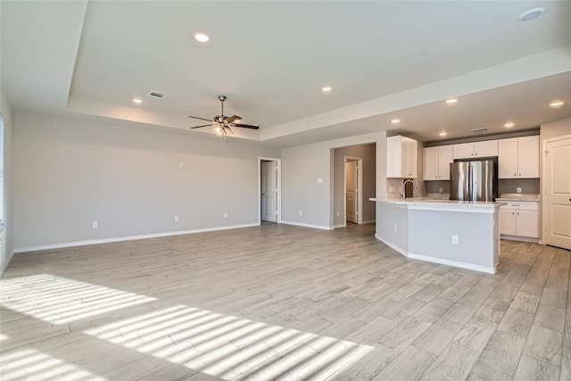 kitchen featuring white cabinets, a raised ceiling, stainless steel fridge, and light wood-type flooring