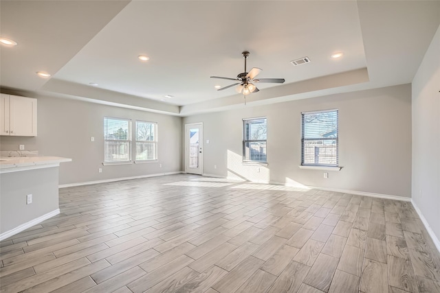 unfurnished living room featuring a tray ceiling, light hardwood / wood-style flooring, and ceiling fan